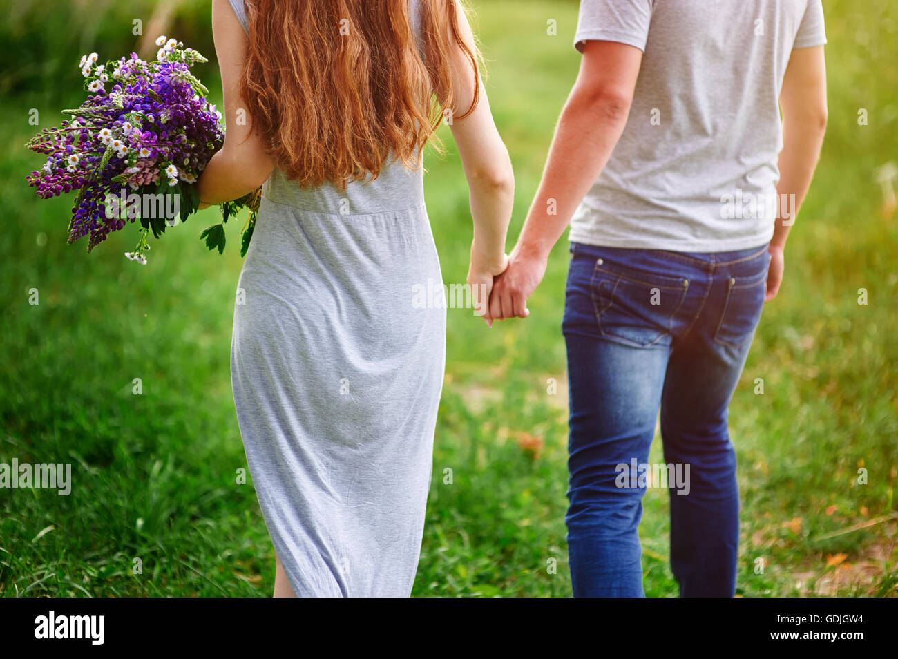 couple walking on meadow with bouquet of flowers Stock Photo