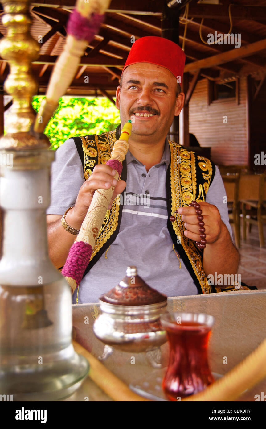Man wearing fez hat, smoking narghile at Neveshir, Turkey. A hookah