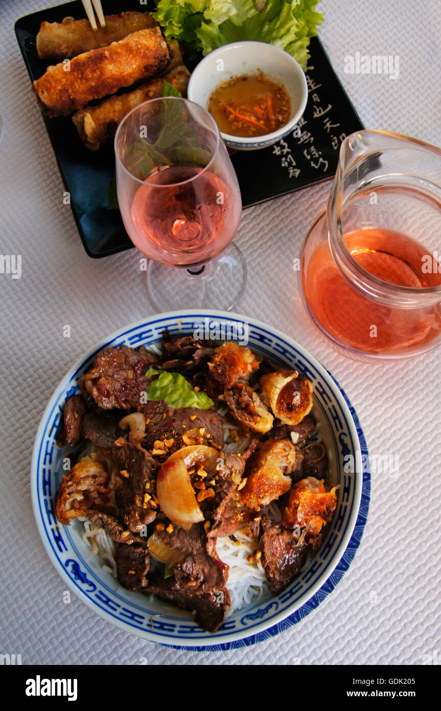 "Nem" (Vietnamese spring rolls) and beef and chicken salad, with rosé wine, Oriental food. Stock Photo