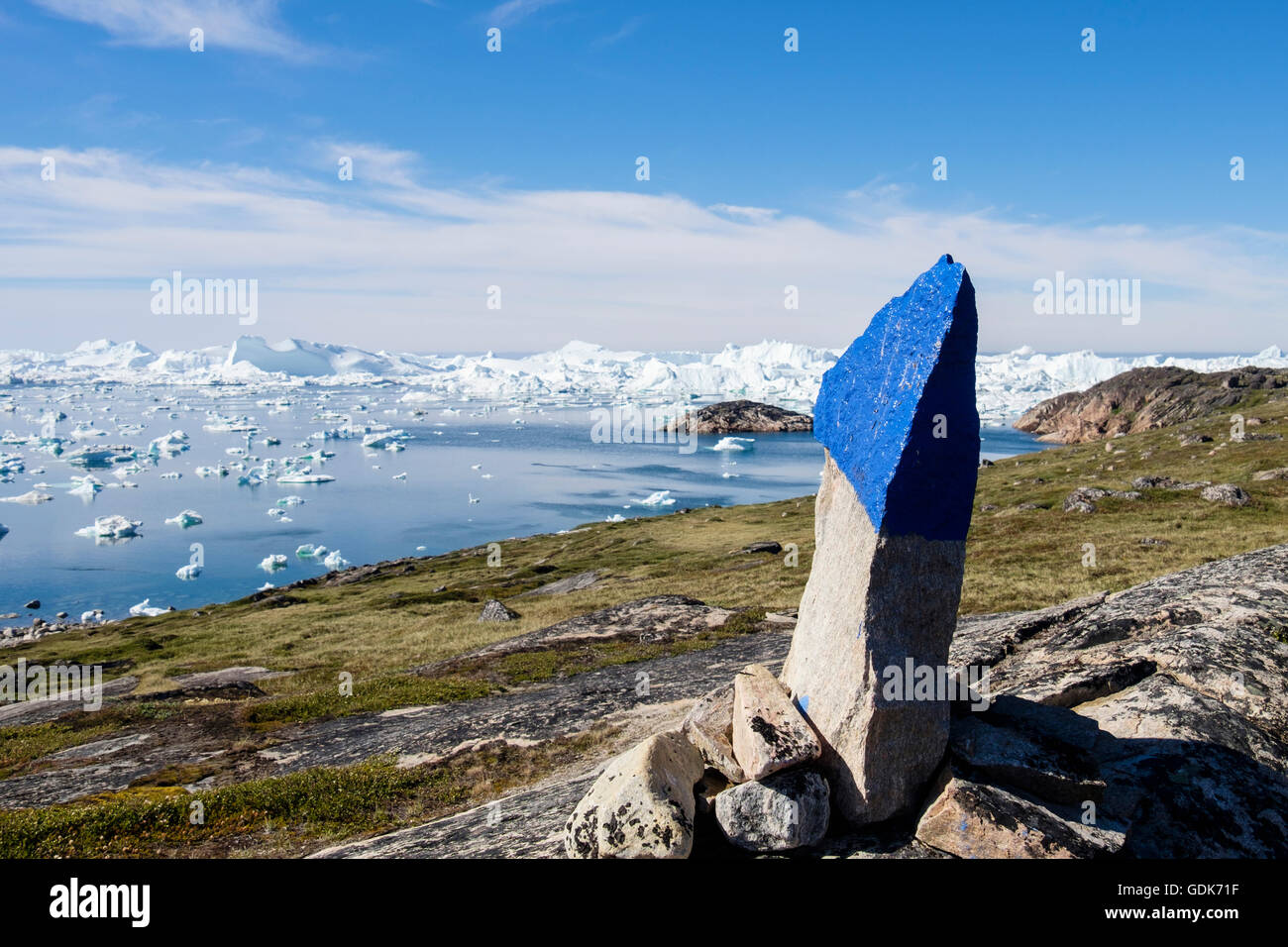 Painted stone cairn marking blue trail beside Ilulissat Icefjord with icebergs in fjord in summer. Ilulissat Western Greenland Stock Photo
