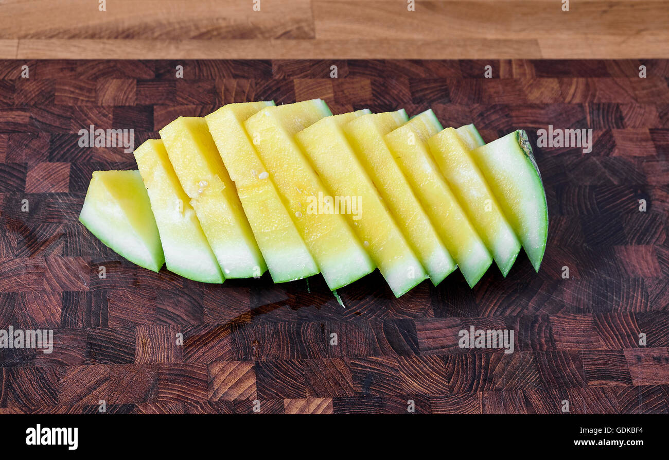 Yellow watermelon sliced in pieces, lying on a table of dark brown laminated hardwood Stock Photo