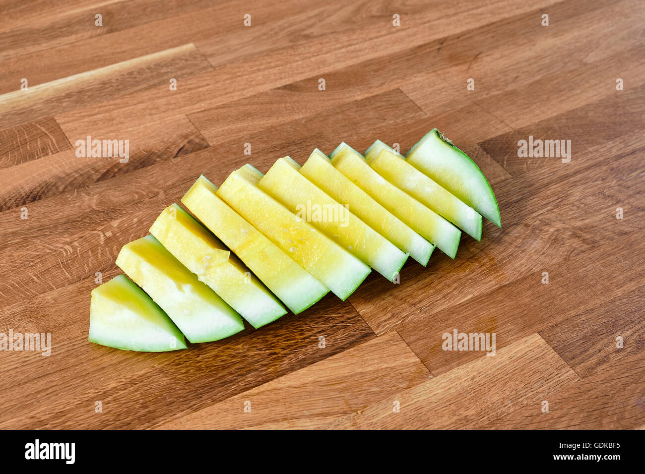 Yellow watermelon sliced in pieces, lying on a table of dark brown laminated hardwood Stock Photo