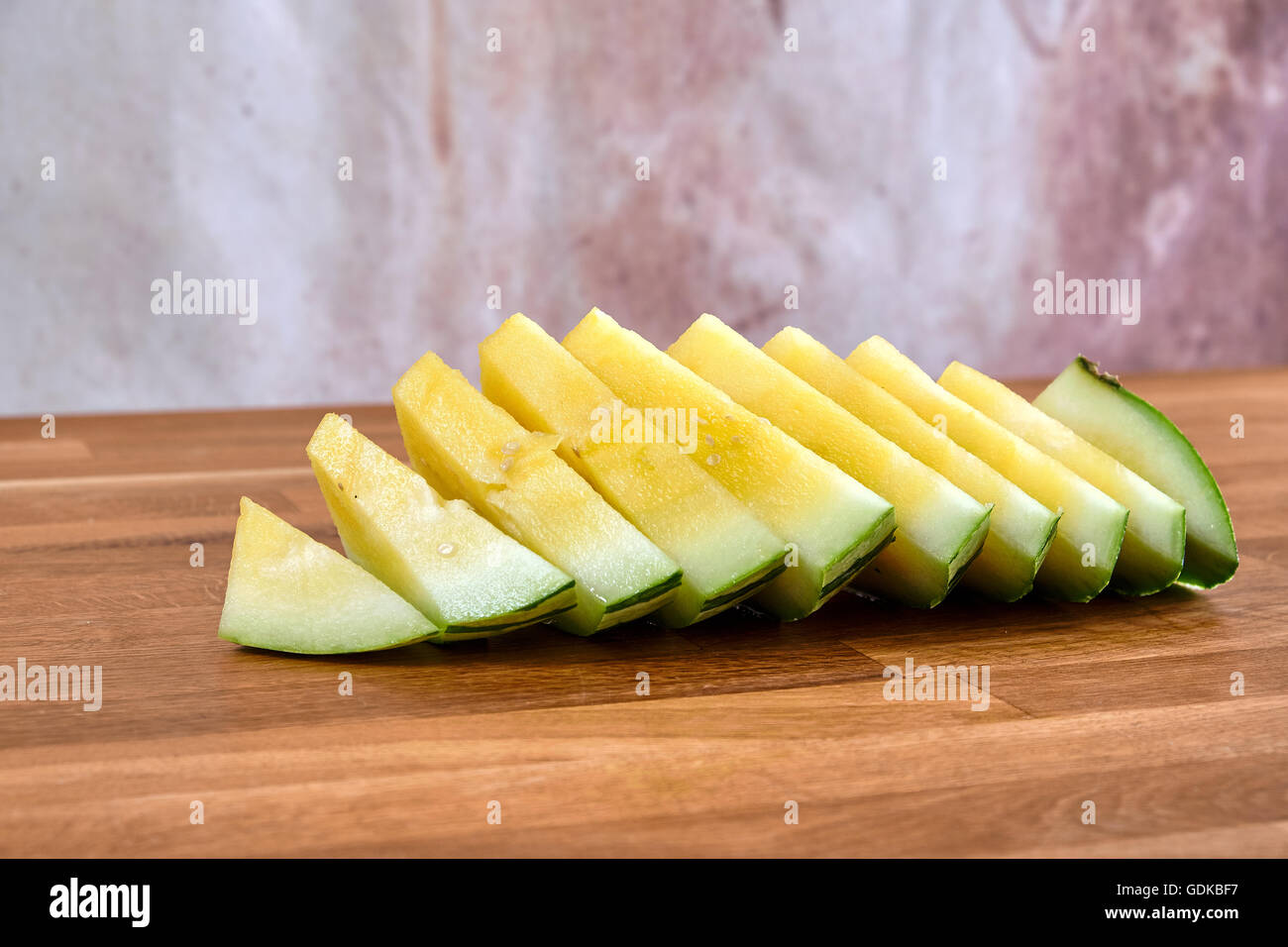 Yellow watermelon sliced in pieces, lying on a table of dark brown laminated hardwood Stock Photo