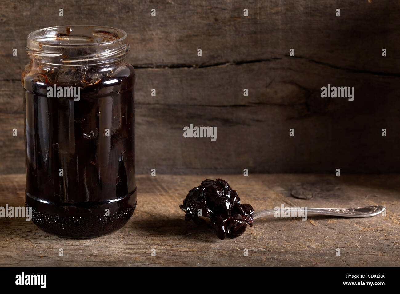 Cherry jam in a preserving glass and spoon over old wooden rustic background Stock Photo