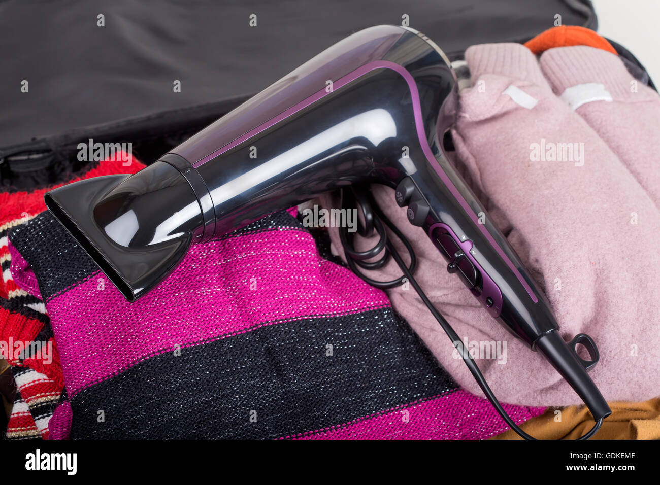 Modern hair dryer on travel bag with clothes Stock Photo