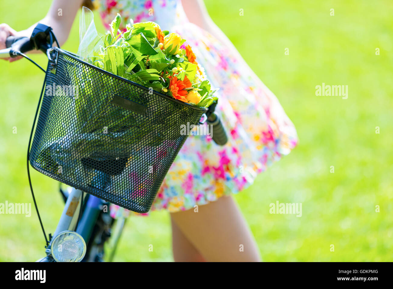 Girl in color short dress stands near bike with basket and flower bouquet Stock Photo