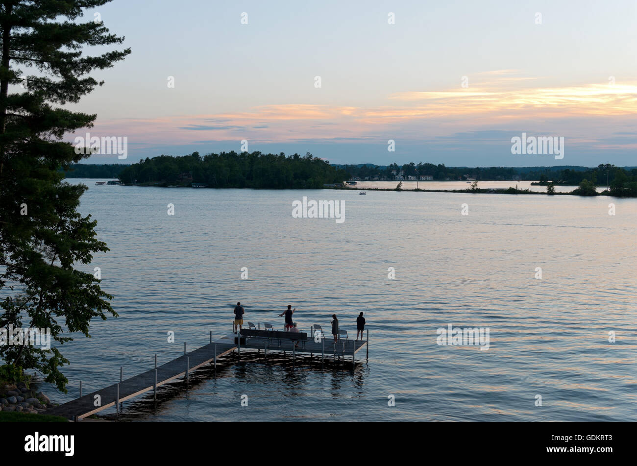 pier with people fishing as sun sets over steamboat bay and birch island of east gull lake in cass county minnesota outside brai Stock Photo