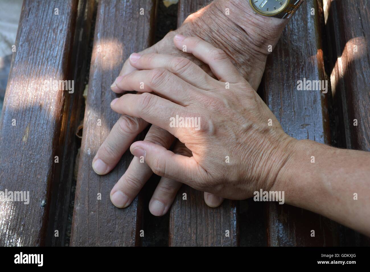 Old and Adult Hands. Hands of a fateher and his daughter on a wooden bench in the street. Stock Photo