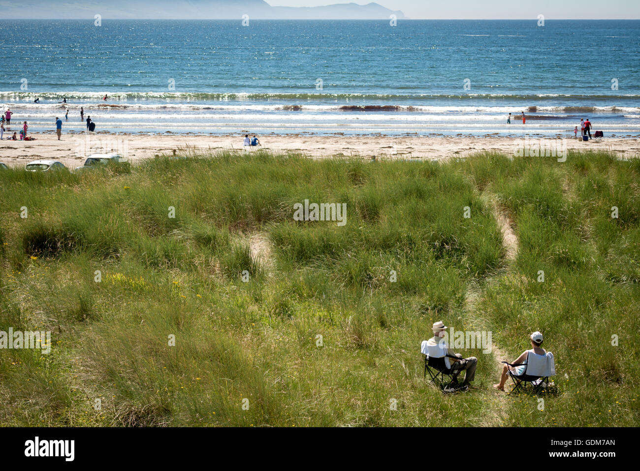 Heatwave Ireland and happy retirement concept as old seniors couple sitting close to the sea on a sandy grass dune at Inch Beach, County Kerry, Ireland Stock Photo