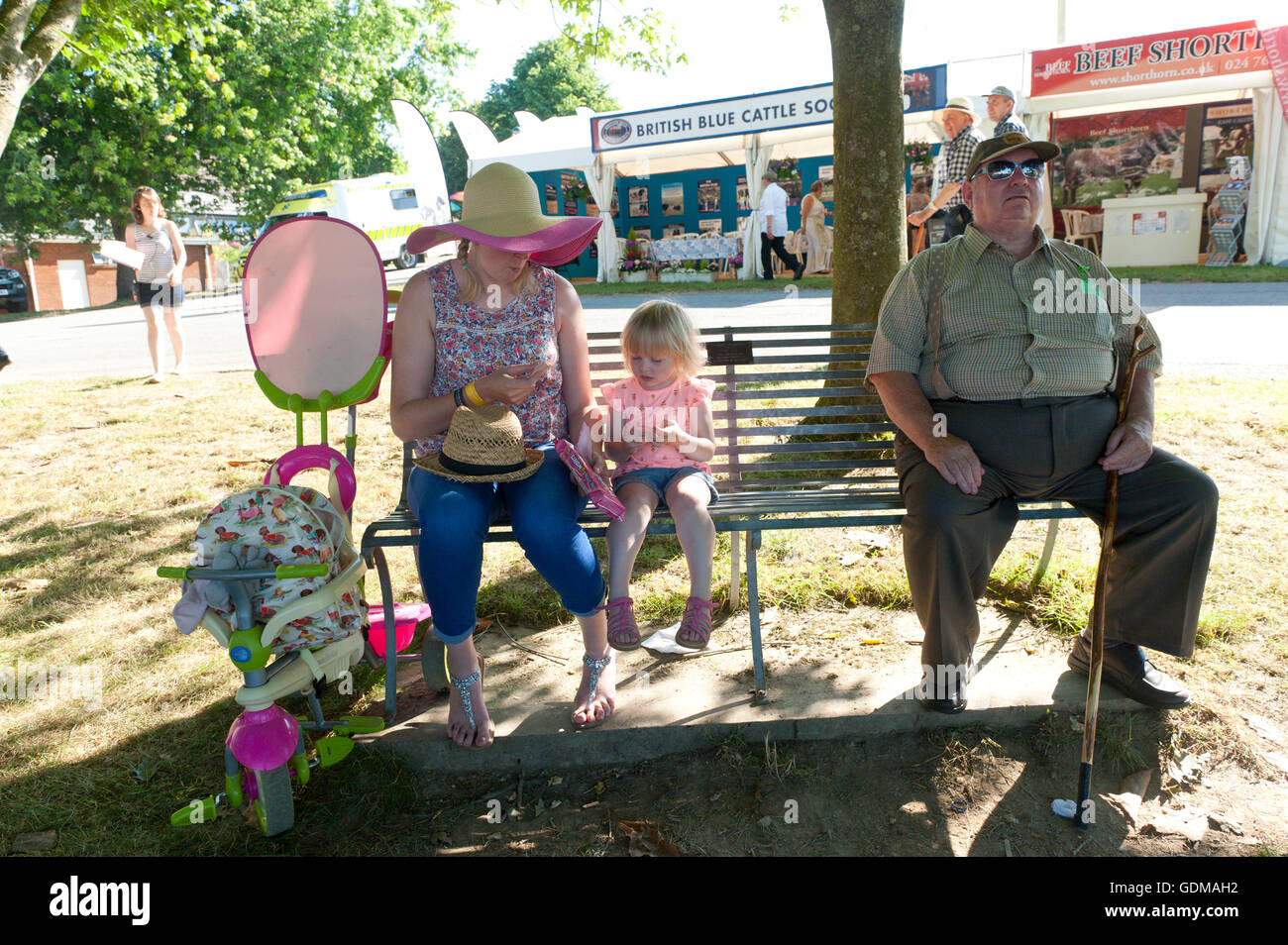 Llanelwedd, Powys, UK. 19th July 2016. Angharad (L) teaching assistant from Llandysul, Wales, and her daughter 2 1/2 -year-old daughter Madi, take refuge in the shade of trees near the cattle ring on the 2nd day of the Royal Welsh  Agricultural Show 2016 with forecasts of temperatures in the high 20 degrees centigrade. Credit:  Graham M. Lawrence/Alamy Live News. Stock Photo