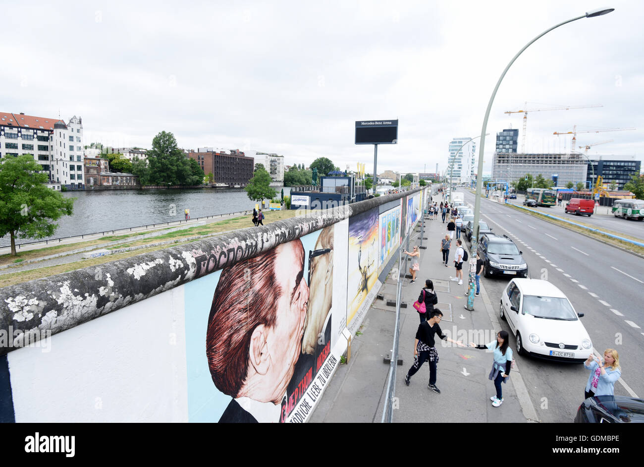 Tourists stand at the painting 'Fraternal Kiss betwen Leonid Breschnew and Erich Honecker' (also often called 'My God, Help Me to Survive This Deadly Love') by Dmitri Wladimirowitsch Wrubel at the East Side Gallery in Berlin, Germany, 19 July 2016. Since a few months the monument on the former inner-German border has been repaired and renovated due to numerous smearings on the artwork. The fence is meant to protect the painting from renewed damage by visitors. The local administration office Friedrichshain-Kreuzberg plans continuing to protect the artwork even after the renovation works. Photo Stock Photo