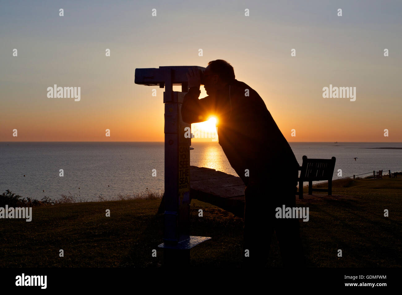 Tankerton, Kent, UK 20th July 2016: UK Weather. The sun rises into a hazy but cloudless sky as a man watches through viewing binoculars at Tankerton slopes near Whitstable in Kent after a night where temperatures did not fall below 22°C. The weather is set to cool down with showers forecast for Thursday Credit:  Alan Payton/Alamy Live News Stock Photo