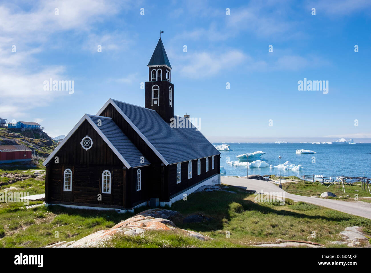 18th century wooden Zions Kirke or Zion Church overlooking Disko Bay with icebergs floating offshore in summer. Ilulissat West Greenland Stock Photo