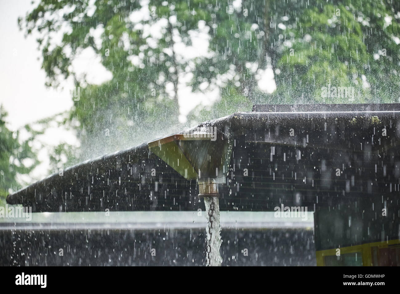 Heavy rain pours in to a big conductor box from where it runs out and down a chain made of metal rings Stock Photo