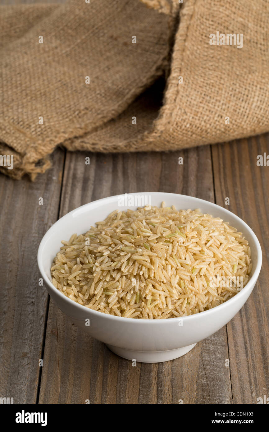 Natural brown uncooked rice in white bowl on wooden table Stock Photo