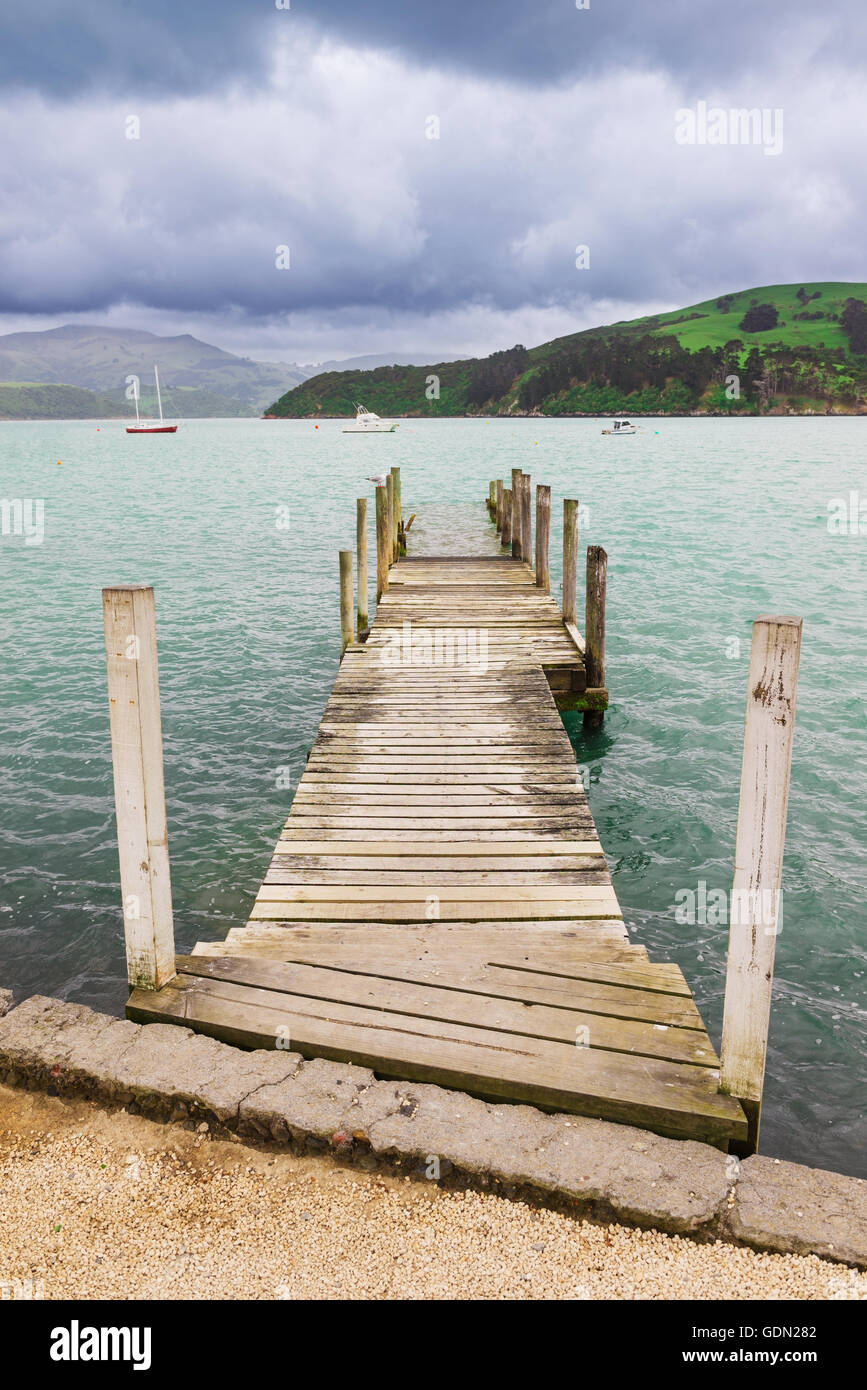 Old wooden pier jetty over the sea shore at Akaroa, New Zealand Stock Photo