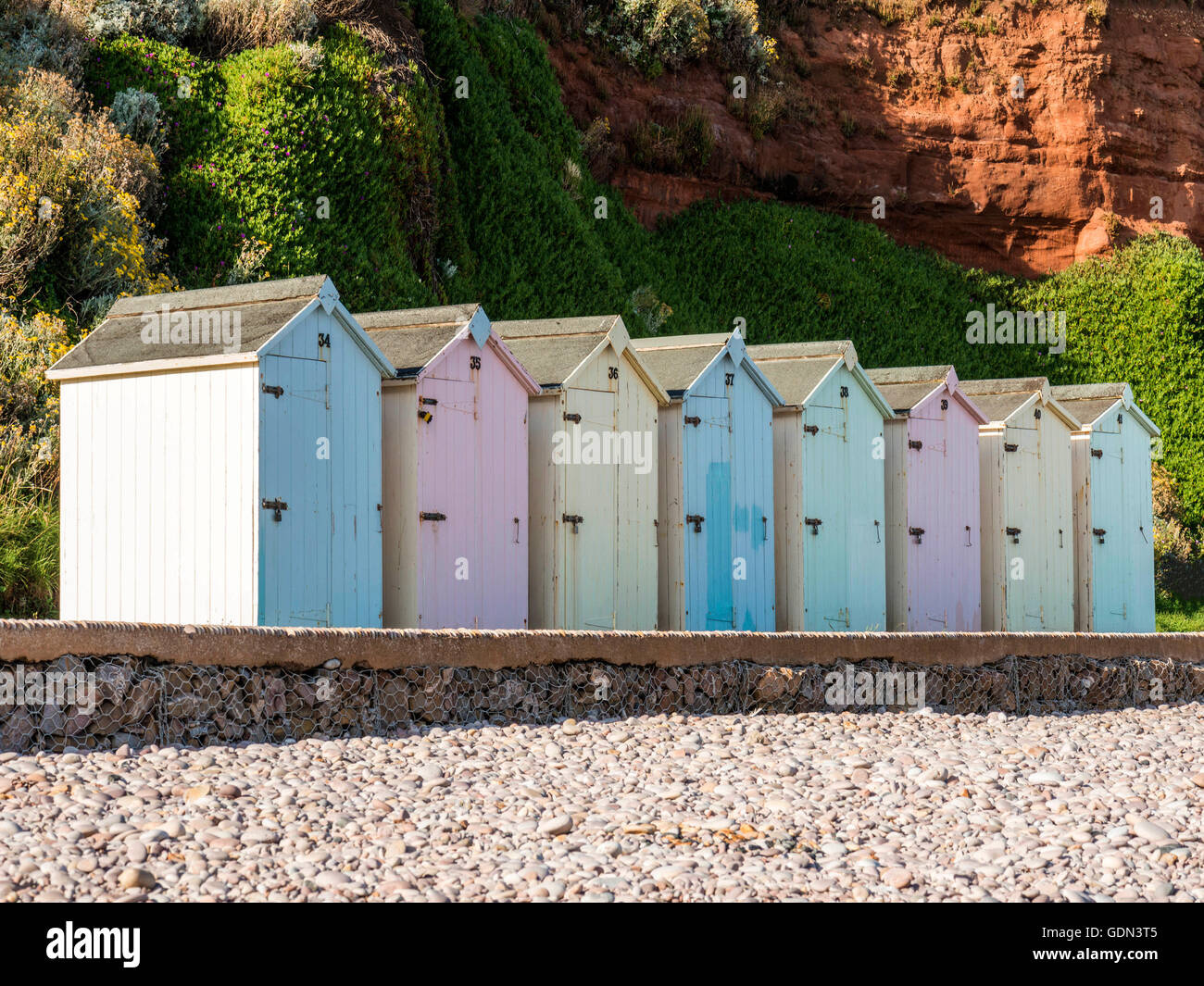 Seaside scene depicting a row of multicolored beach huts, asphalt pathway, pebbled beach and Jurassic coast. Stock Photo