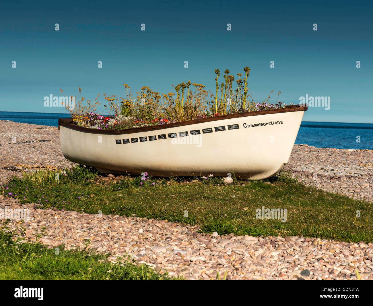 Seaside summer scene, depicting a blue ocean background with commemorative boat in the mid-ground and a pebble beach foreground. Stock Photo