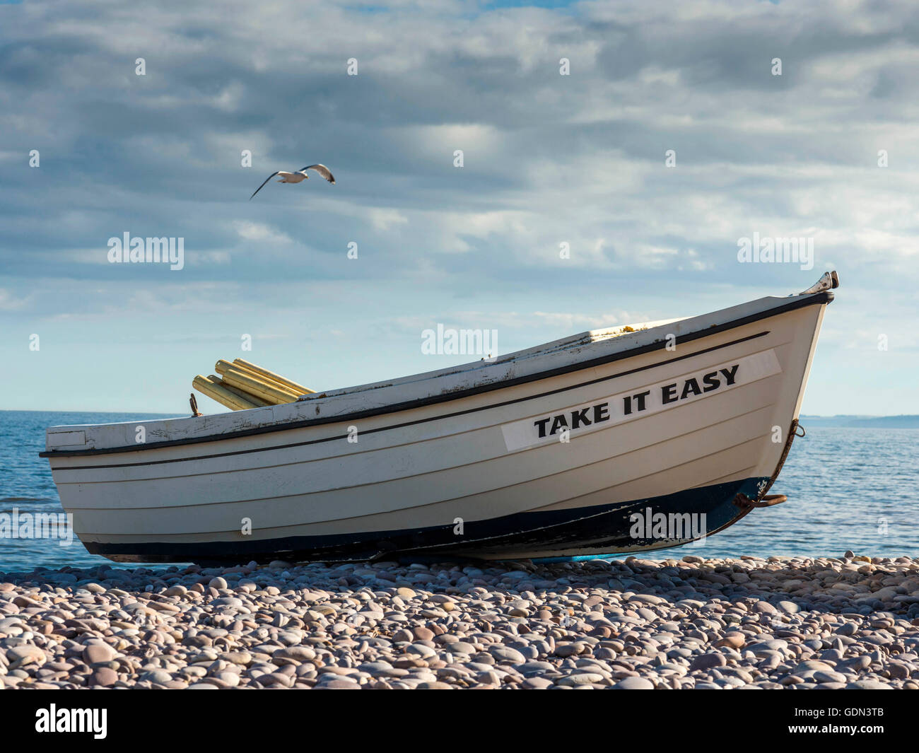 Take It Easy - Seaside scene, depicting a blue ocean background with boat in the mid-ground and a pebble beach foreground. Stock Photo