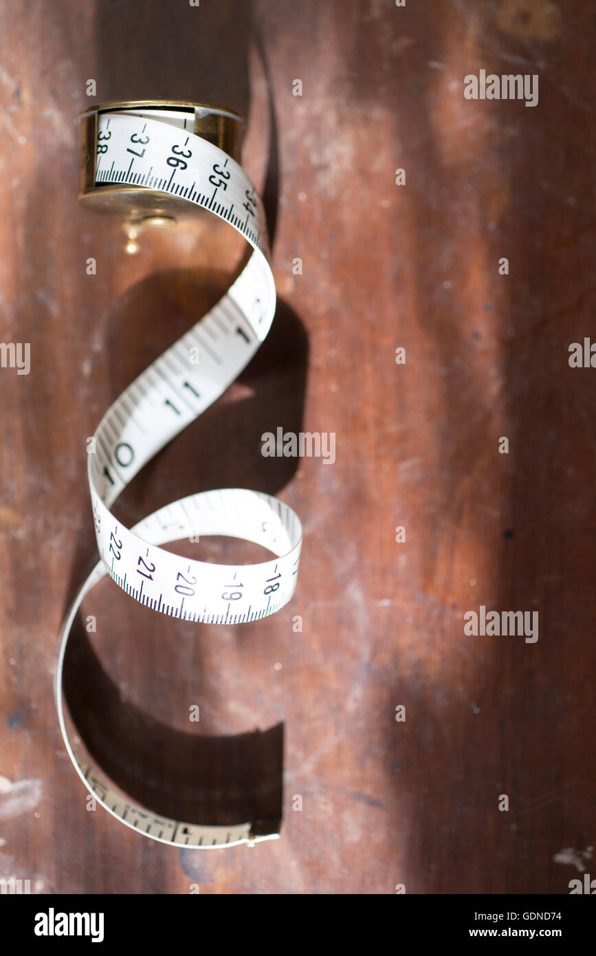 A partly unrolled reel of white tape measure laid on a dark wooden