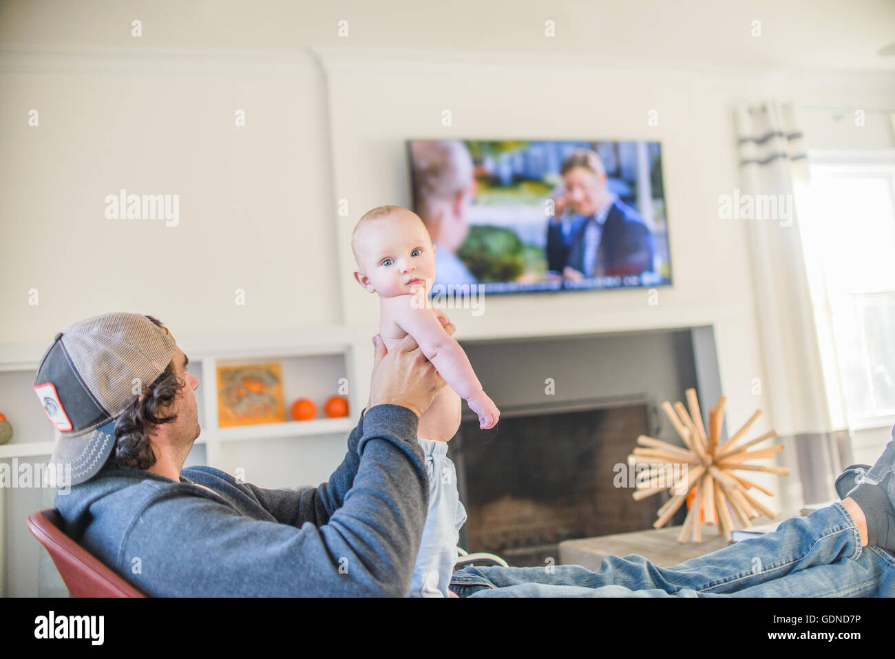 Father watching television holding baby boy Stock Photo