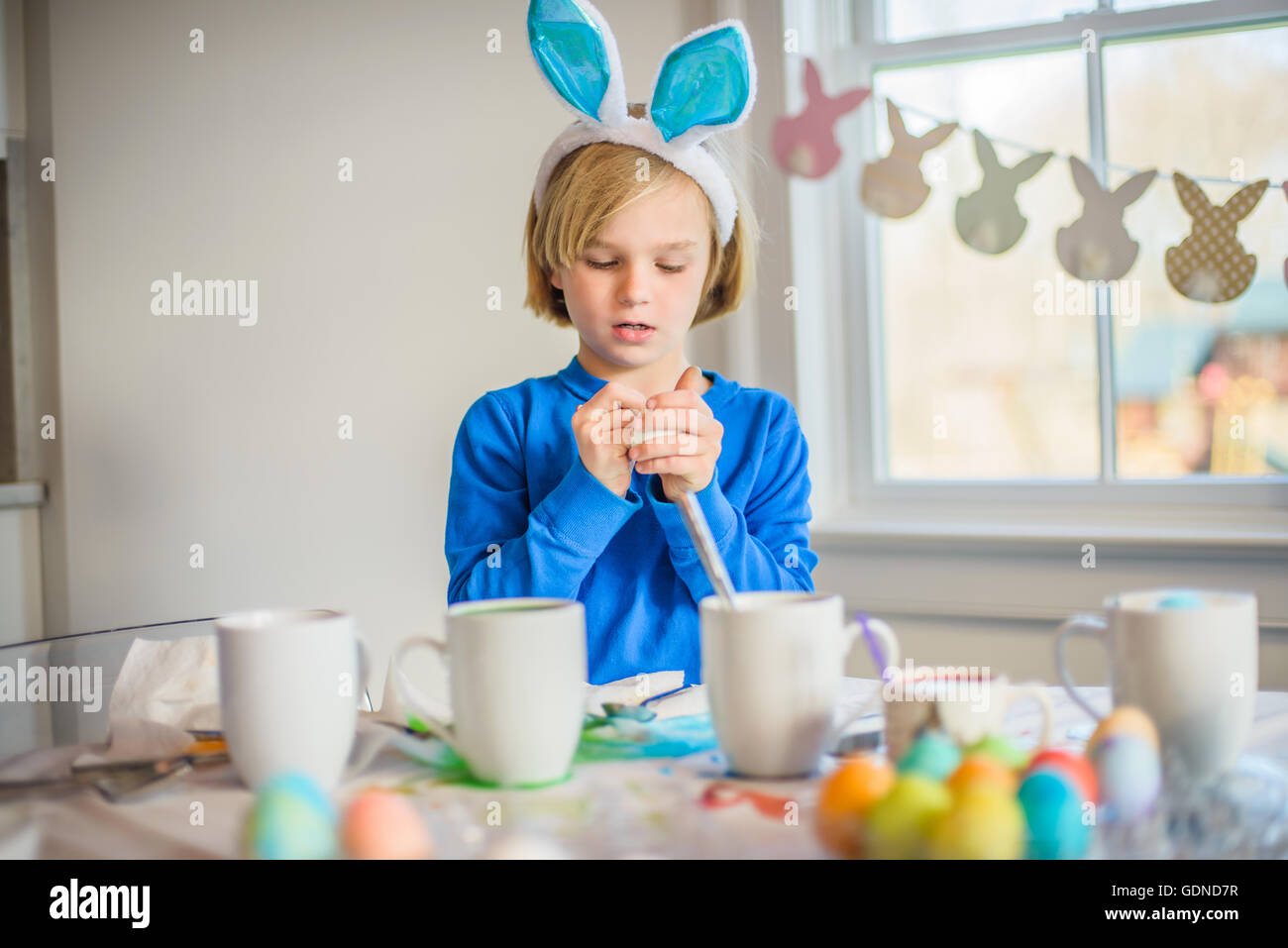 Boy at table wearing bunny ears decorating eggs for Easter Stock Photo