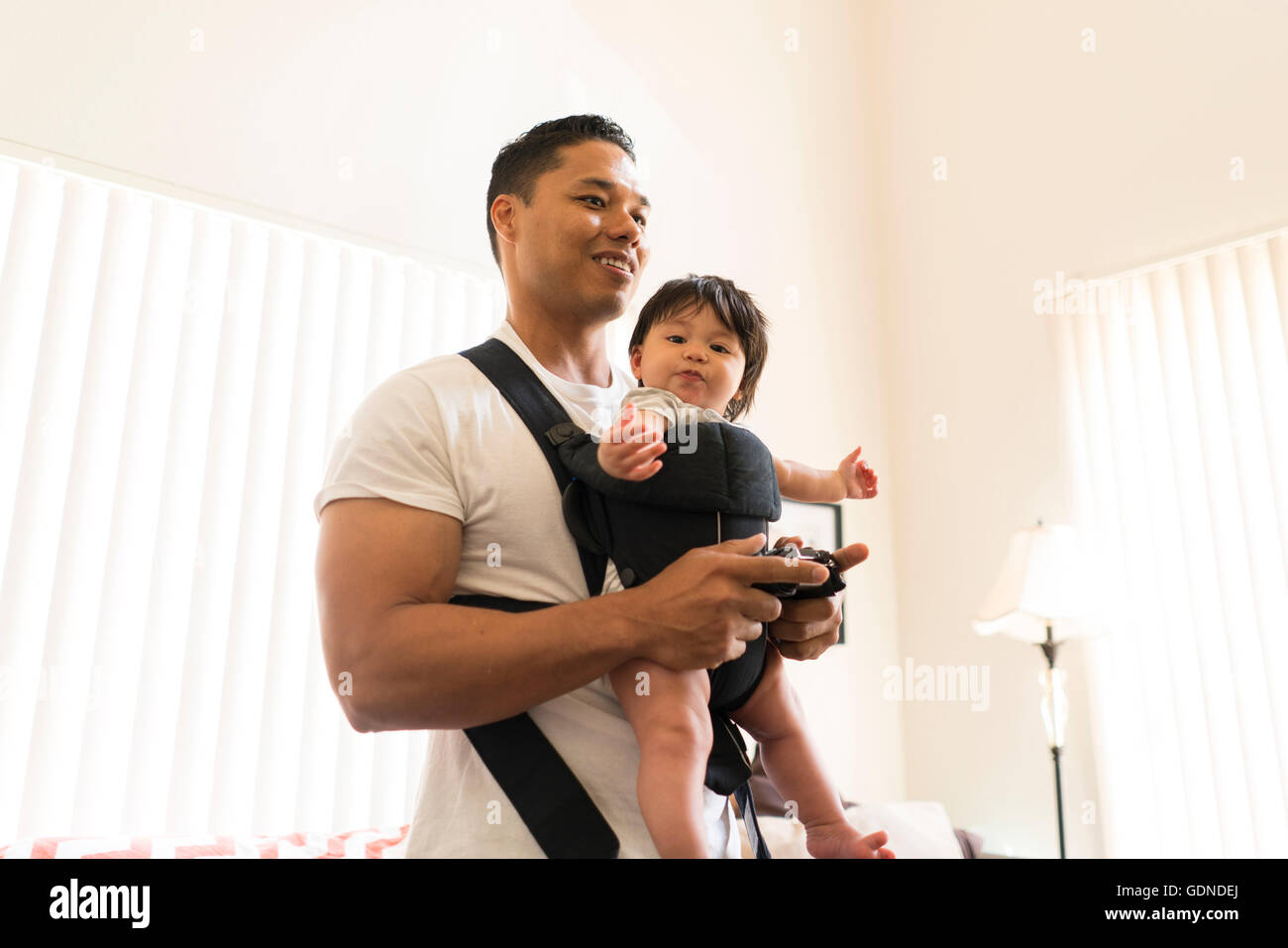 Father with baby in carrier, playing video game Stock Photo