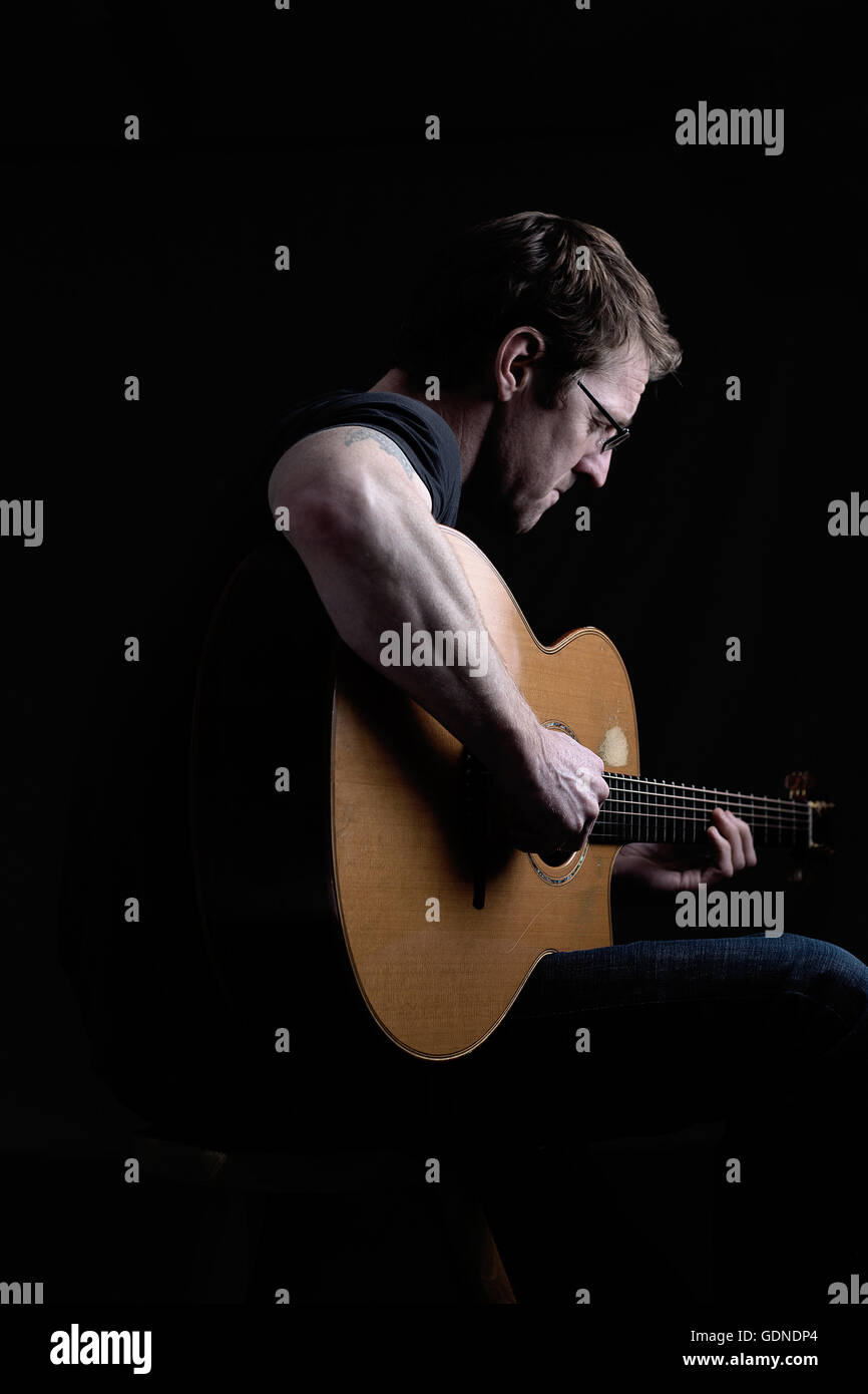 Low key shot of mid adult man playing acoustic guitar Stock Photo