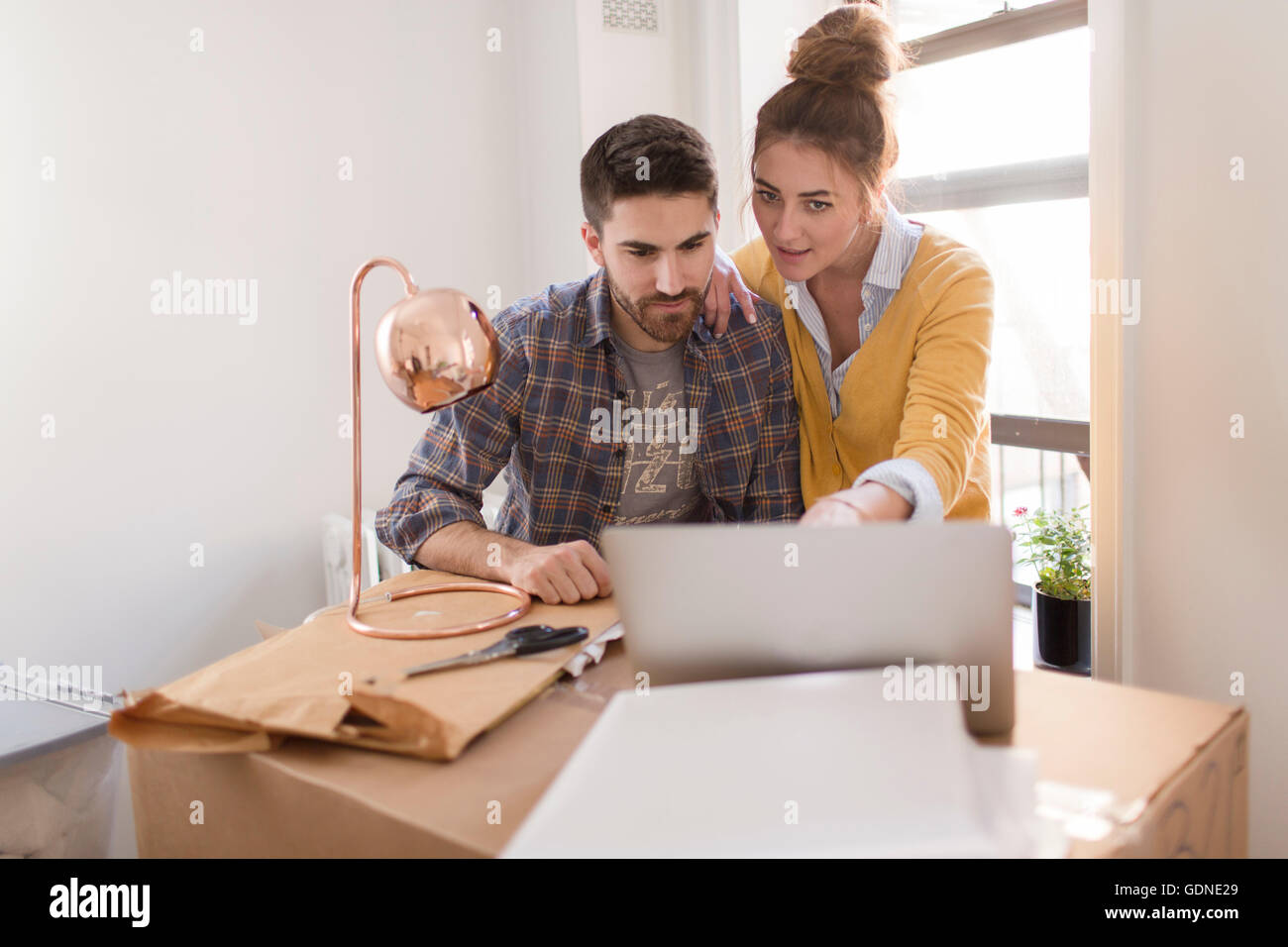 Moving house: Young couple leaning on cardboard box, using laptop Stock Photo