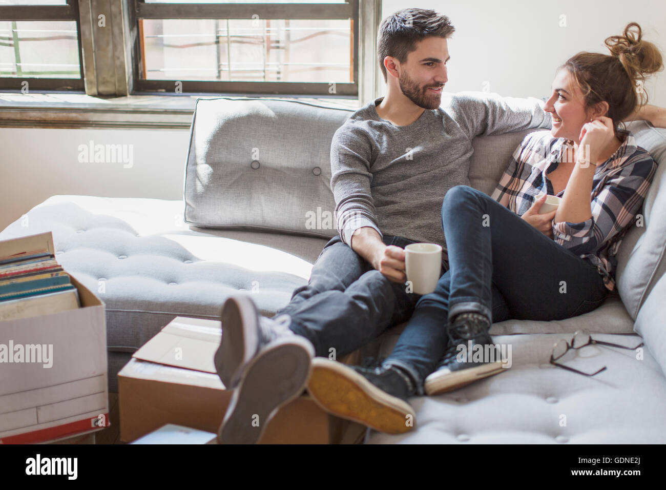 Moving house: Young couple relaxing on sofa surrounded by cardboard boxes Stock Photo