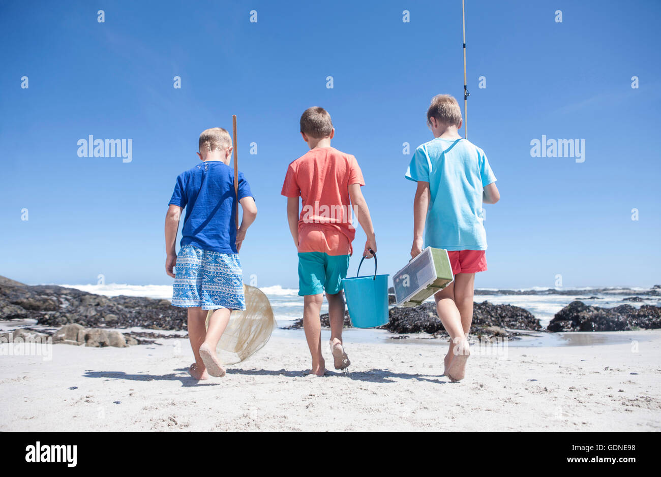 Rear view of three boys walking on beach with fishing net, bucket and