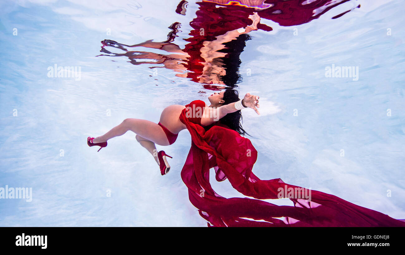 Pregnant woman wearing red high heels and bikini in swimming pool Stock Photo