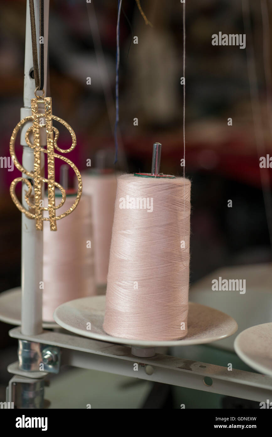 Bobbin of pink thread in a sewing machine spool by a golden dollar sign