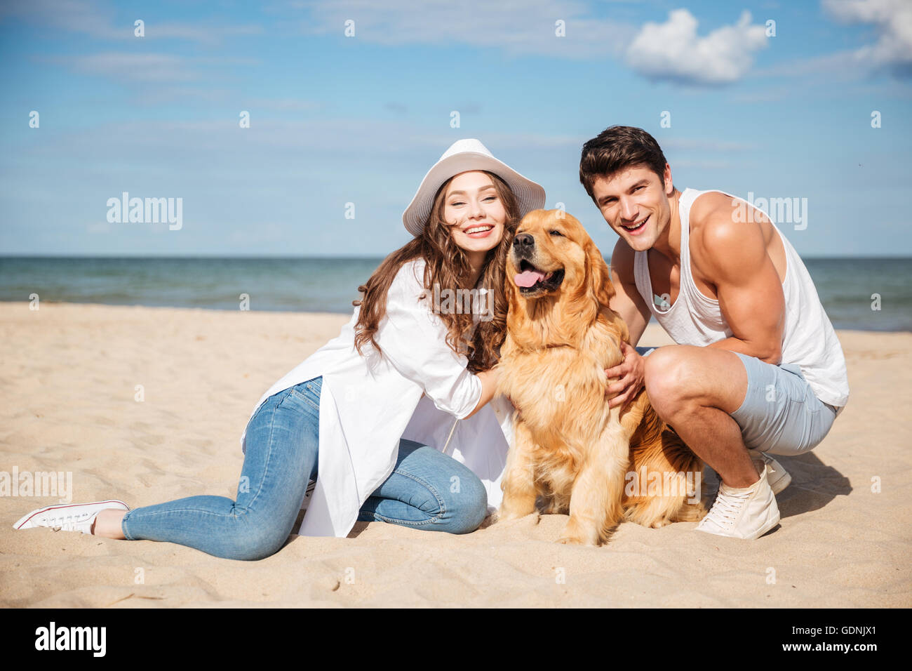 Happy young couple sitting and having fun with dog on the beach Stock ...