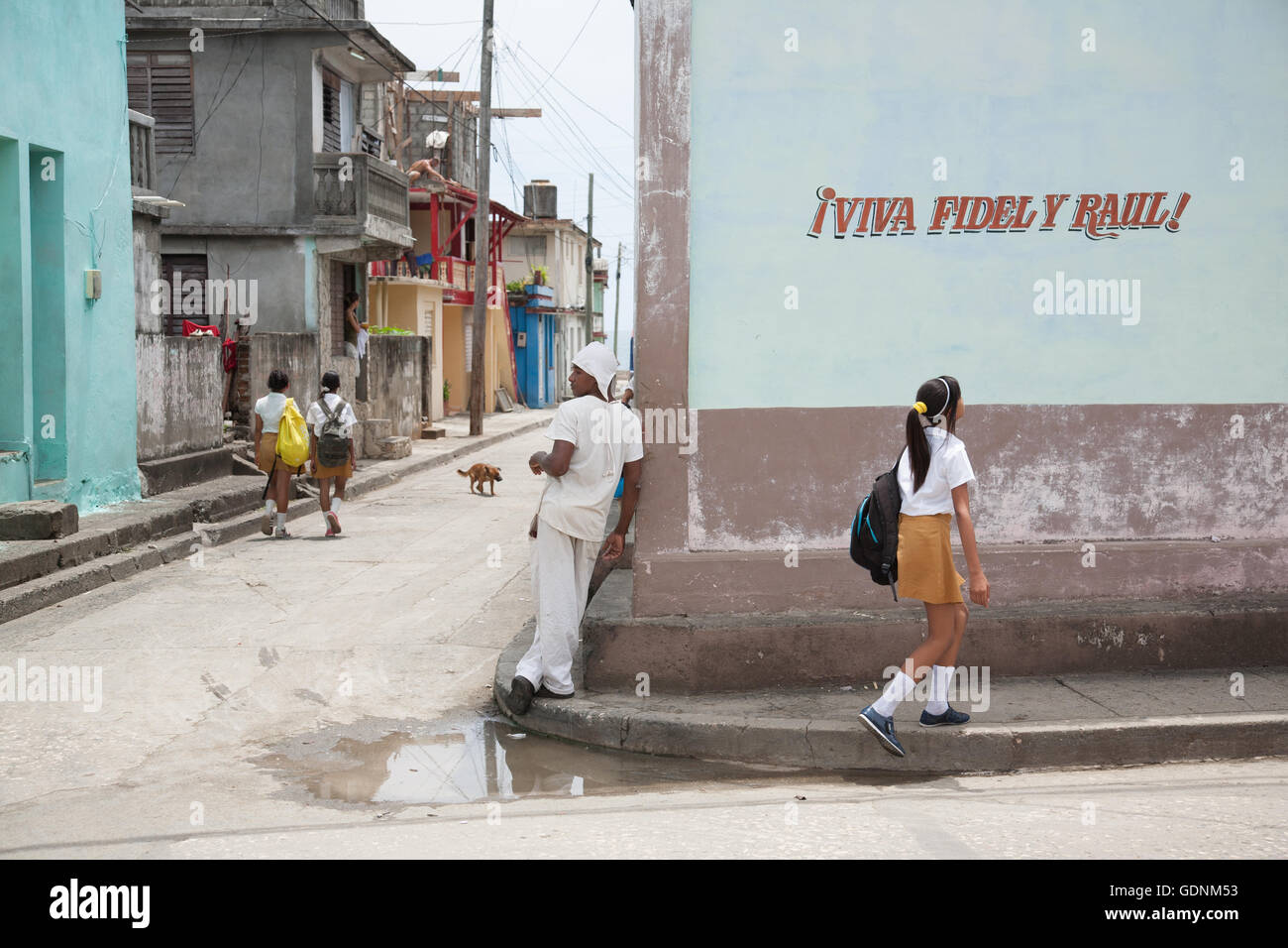 Street scene with a pro-Castro brothers slogan, school children, a baker and a dog, in Baracoa, Cuba Stock Photo