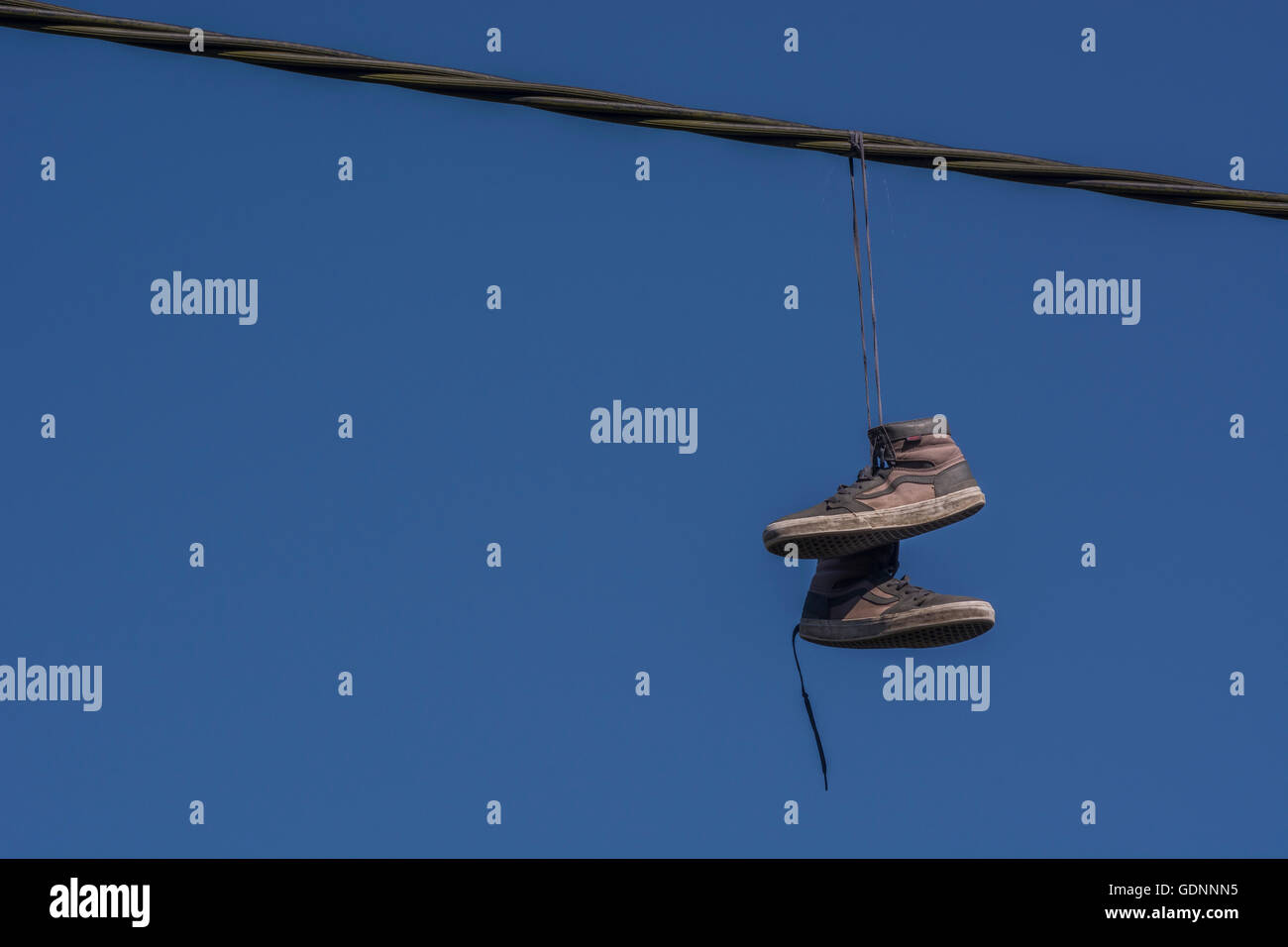 Boots hanging from overhead cable - representing the 'Territorial' concept of drugs, drug dealing turf, & associated addiction, gangland, shoe tossing Stock Photo