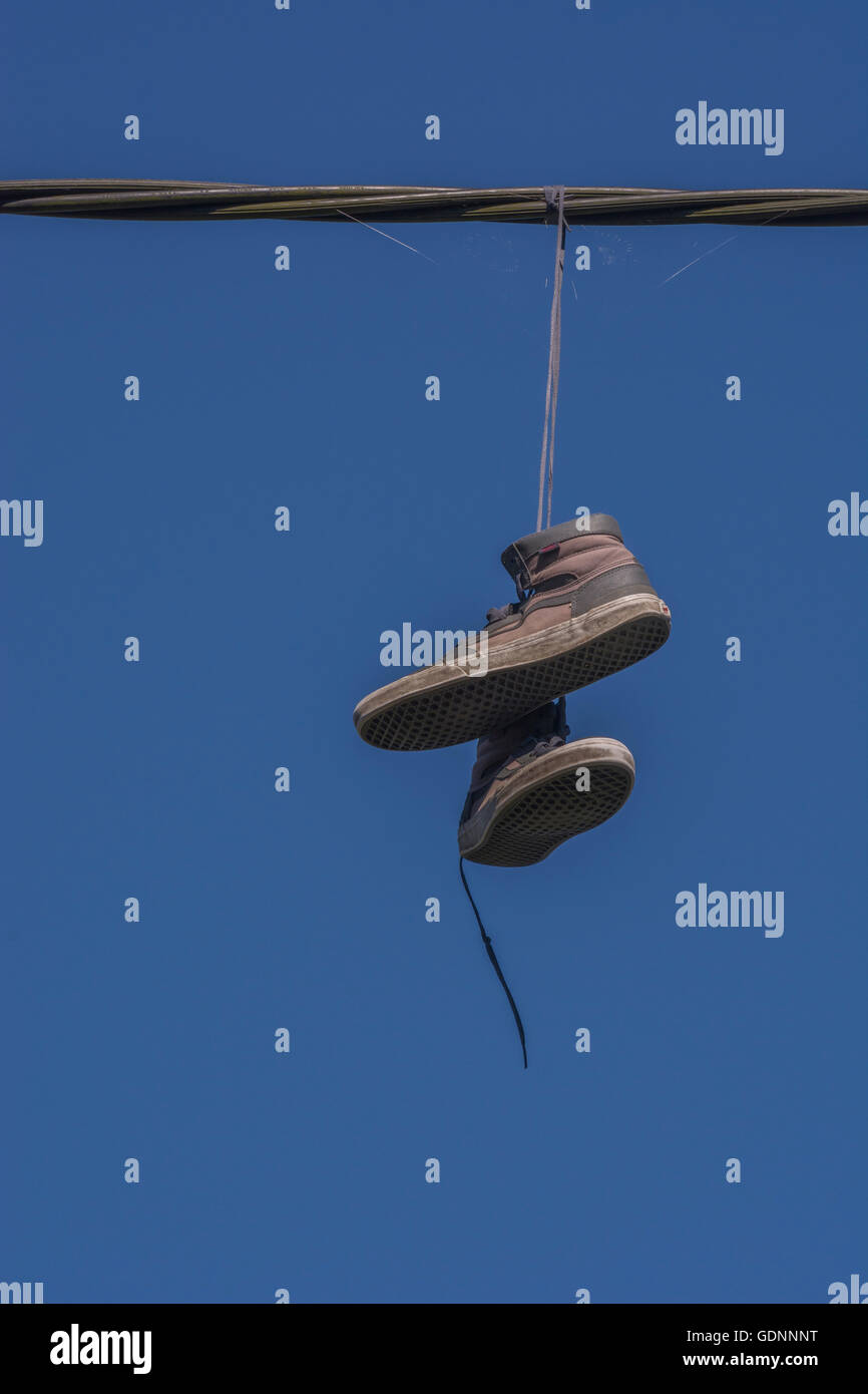 Boots hanging from overhead cable - representing the 'Territorial' concept of drugs, drug dealing turf, & associated addiction, gangland, shoe tossing Stock Photo