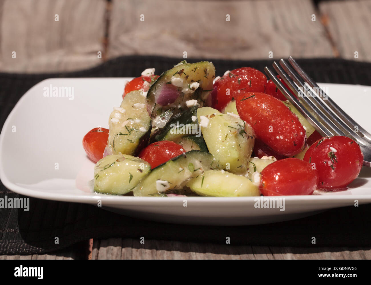 Cucumber, tomato, feta cheese and dill salad with a vinaigrette dressing on a white plate with a fork at mealtime. Stock Photo