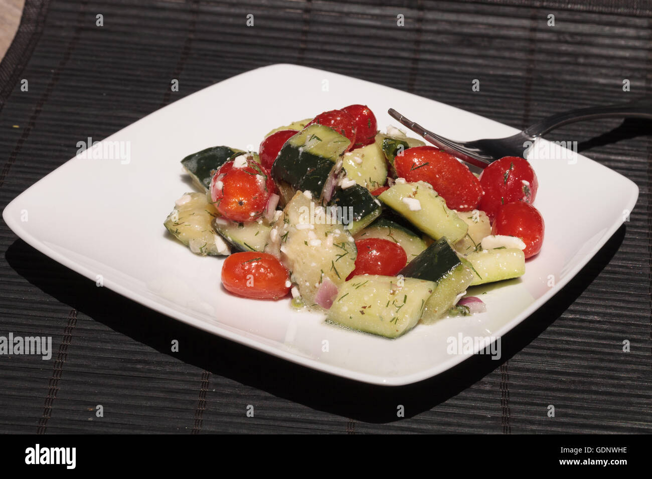 Cucumber, tomato, feta cheese and dill salad with a vinaigrette dressing on a white plate with a fork at mealtime. Stock Photo