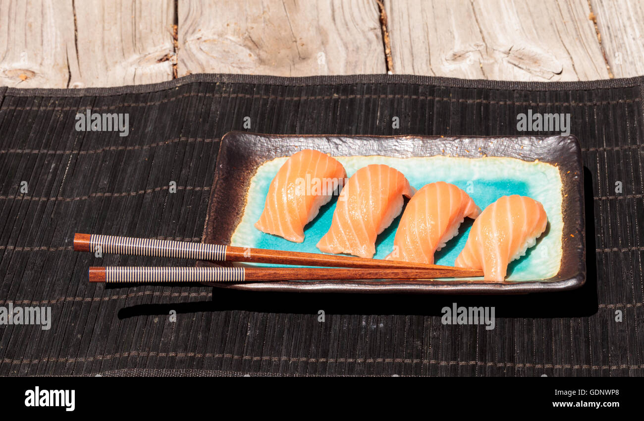 A meal of salmon sushi on white rice on a blue plate with chopsticks. Stock Photo