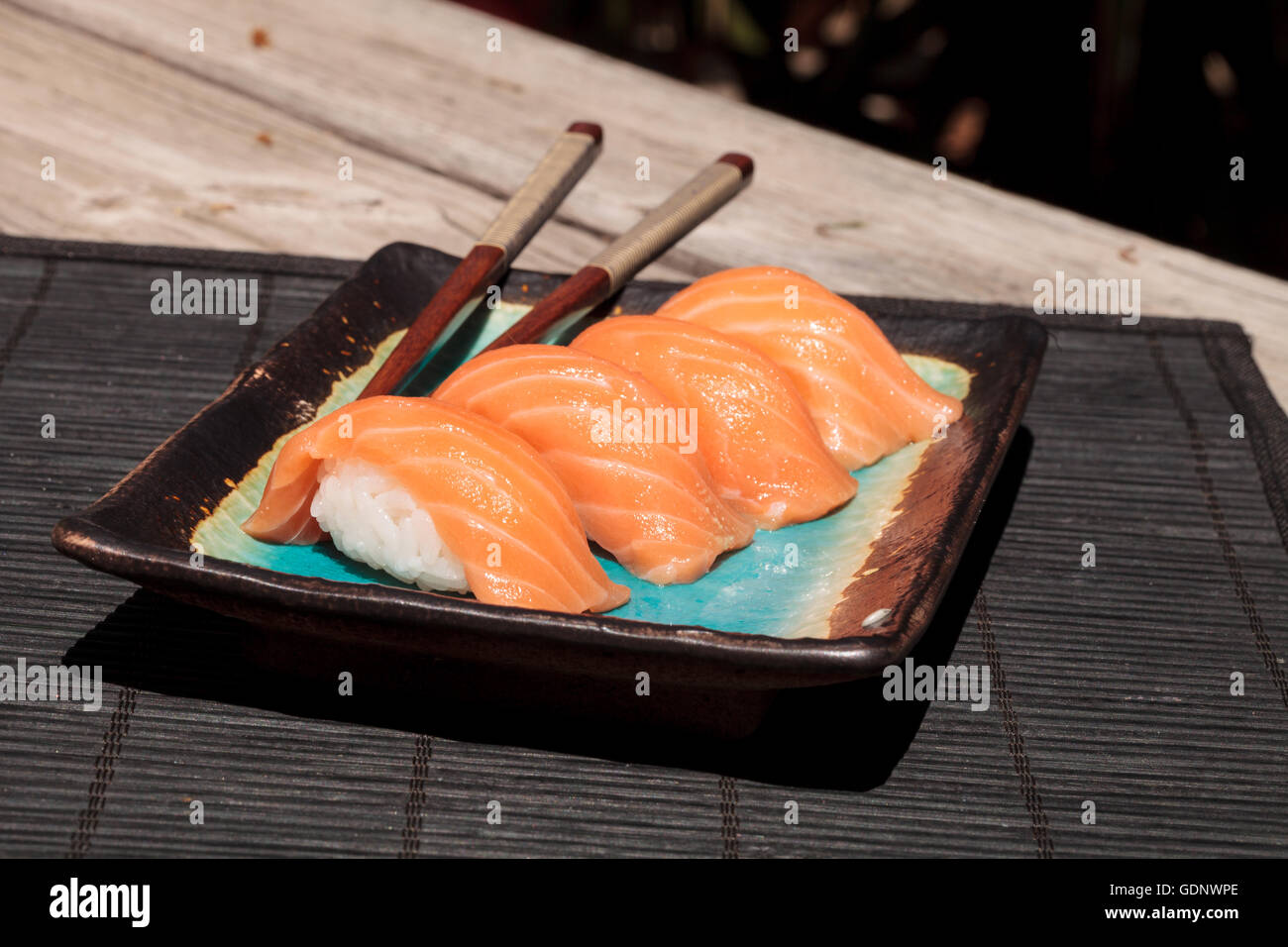 A meal of salmon sushi on white rice on a blue plate with chopsticks. Stock Photo