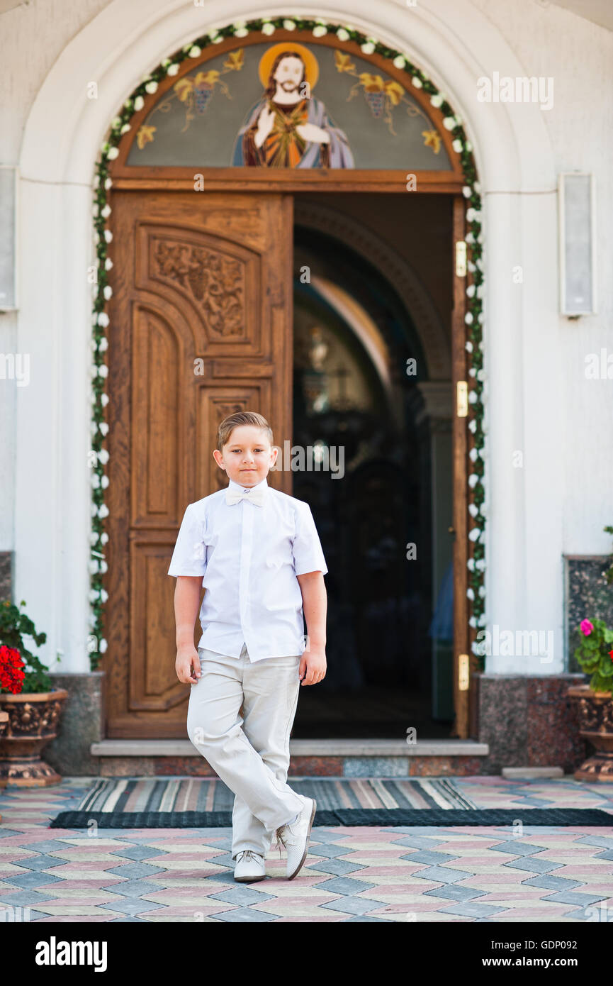 Portrait of little boy on white wear and bow tie on first holy communion background church gate Stock Photo