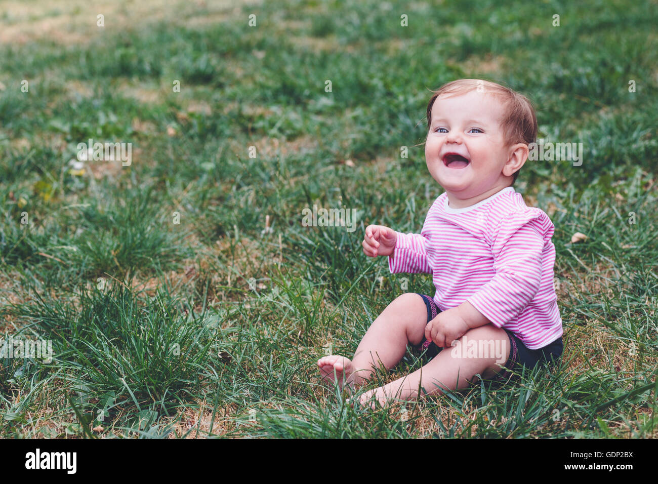 Smiling baby girl sitting on a grass in the garden Stock Photo