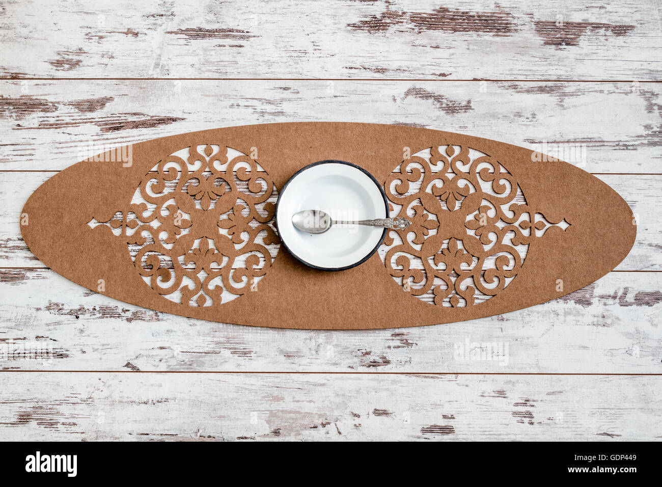 White wooden table set up with enamel plate, spoon and a decorative brown runner Stock Photo