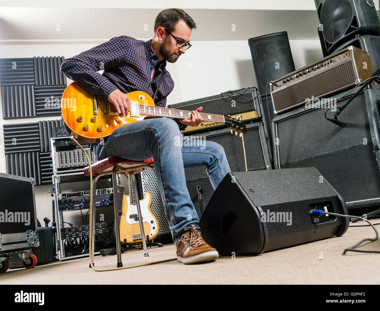 Photo of a man in his late 20's sitting in a recording studio playing his electric guitar. Stock Photo