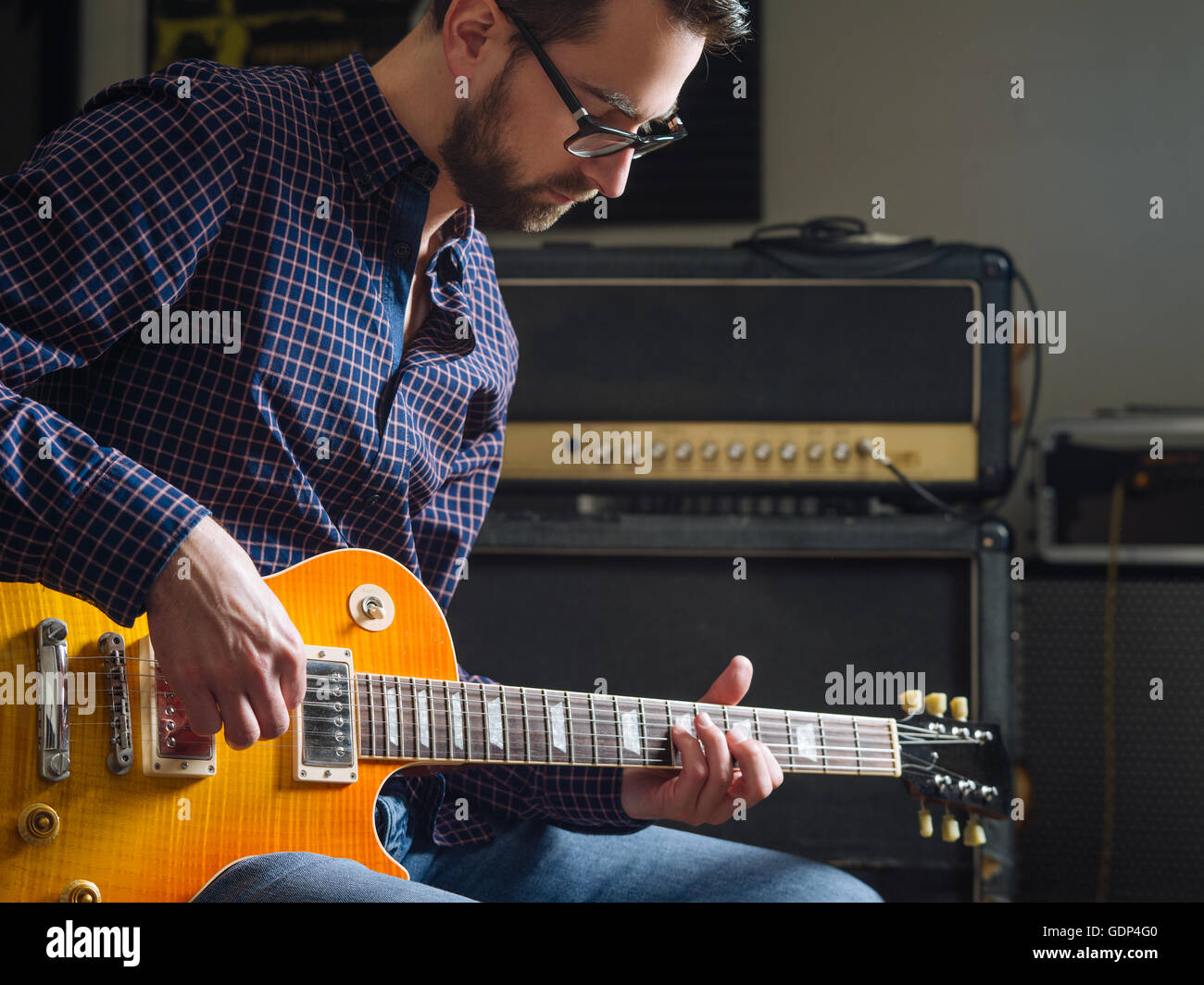 Photo of a man in his late 20's sitting in a studio playing his electric guitar. Stock Photo