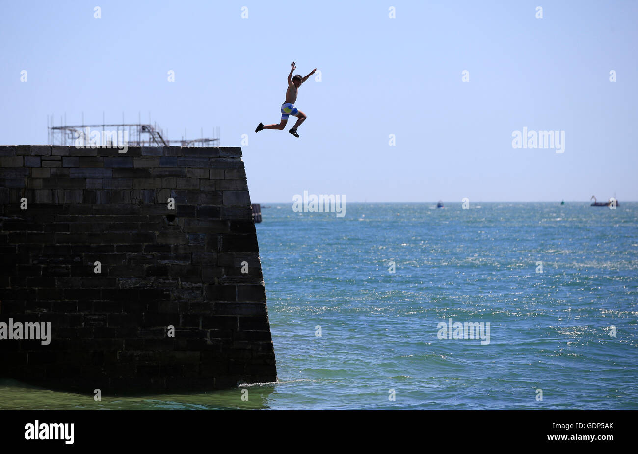 A boy dives off of the sea wall near Old Portsmouth, as Britain has sweltered on the hottest day of the year so far, with soaring temperatures sparking a surge in calls for medical help and causing delays on the railway. Stock Photo