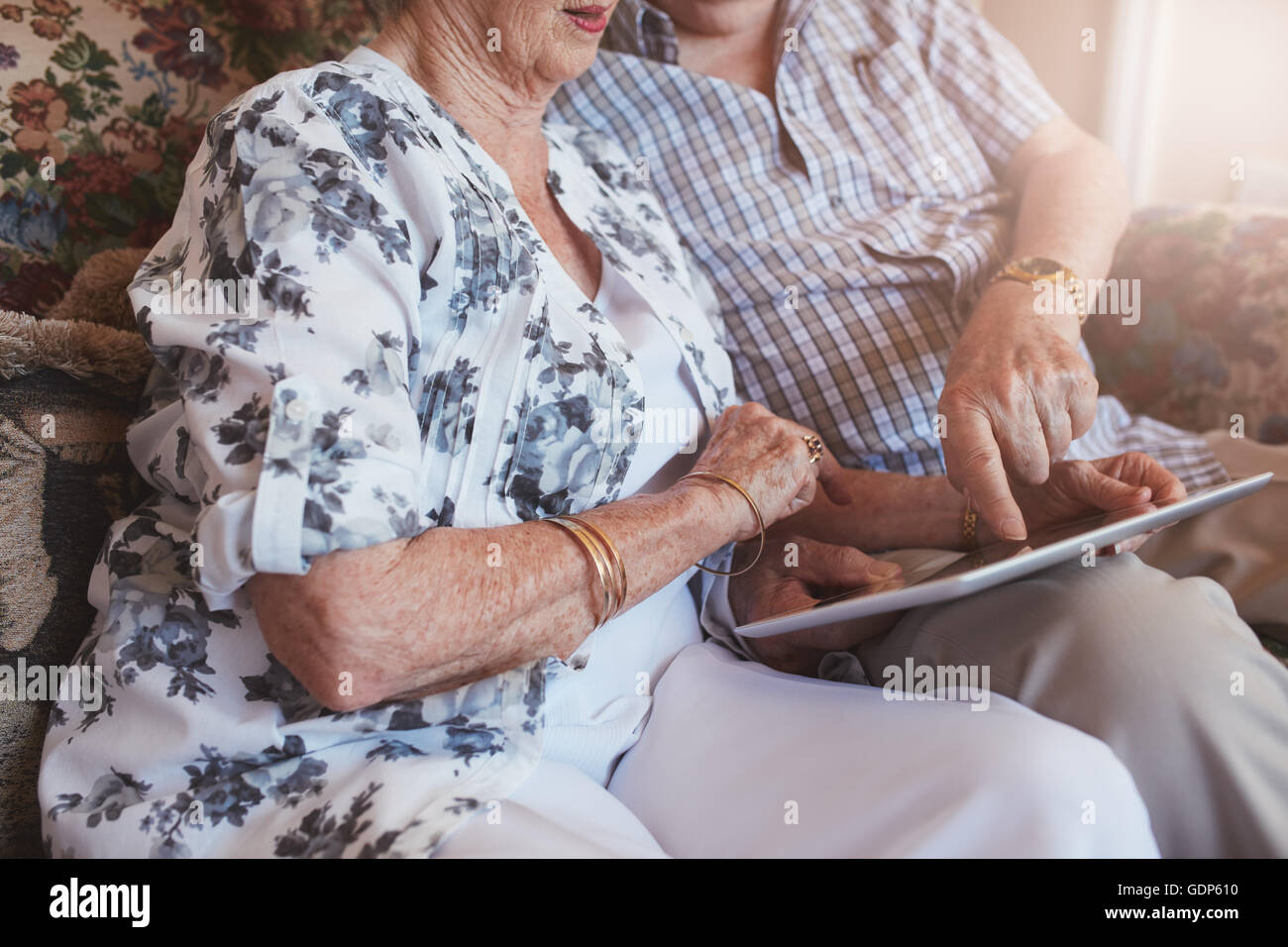 Cropped shot of senior couple sitting together using touch screen computer. Focus on hands of elderly couple and digital tablet. Stock Photo