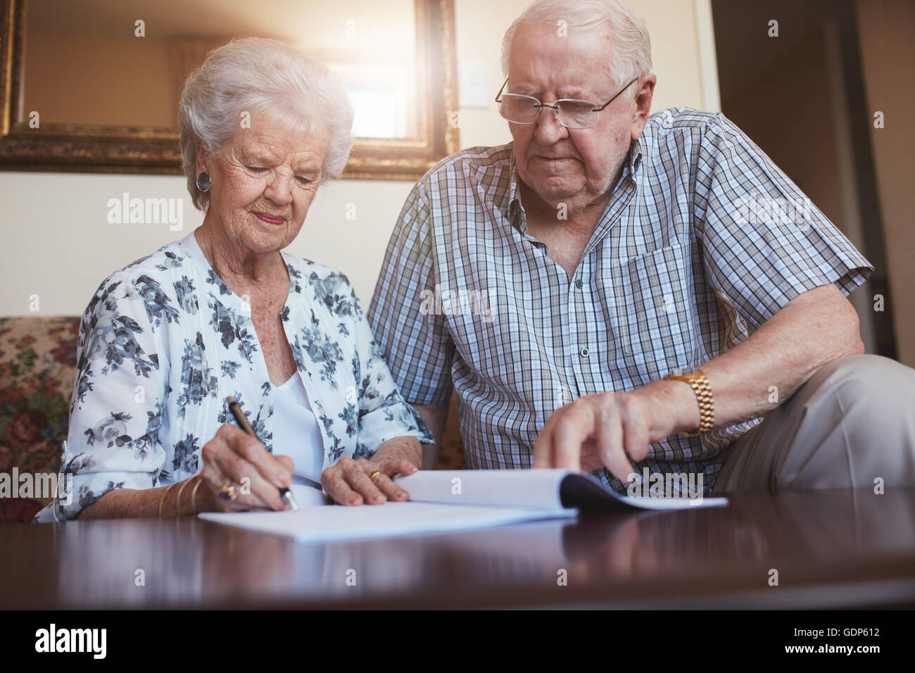 Indoor shot of mature couple at home signing documents together. Senior man and woman sitting on sofa doing retirement paperwork Stock Photo