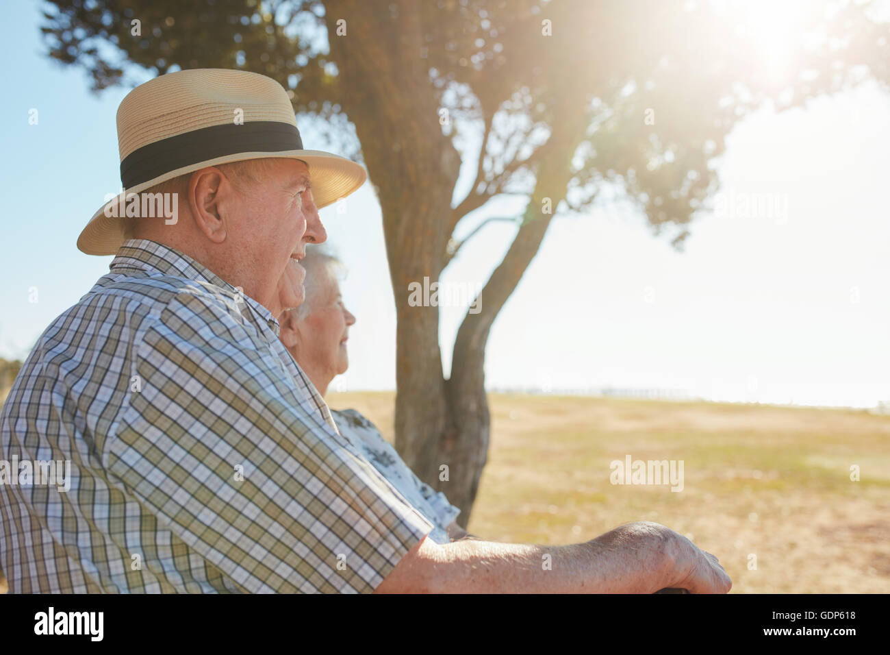 Side view shot of senior man in hat sitting outdoors with his wife and enjoying a view. Elderly couple relaxing outdoors on a su Stock Photo
